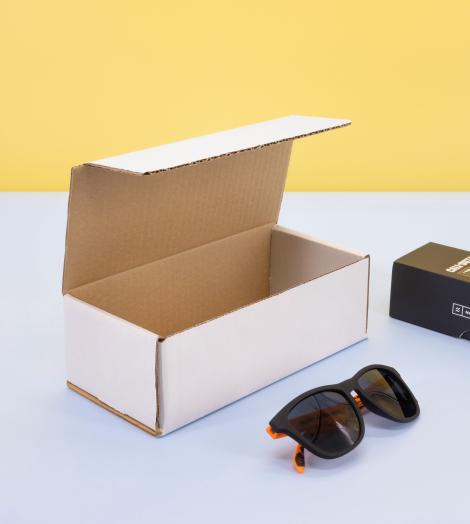 Cajas de cartón pequeñas blancas con gafas de sol y perfume al lado